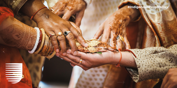An image of people's clasped hands, richly adorned with henna and gold jewellery